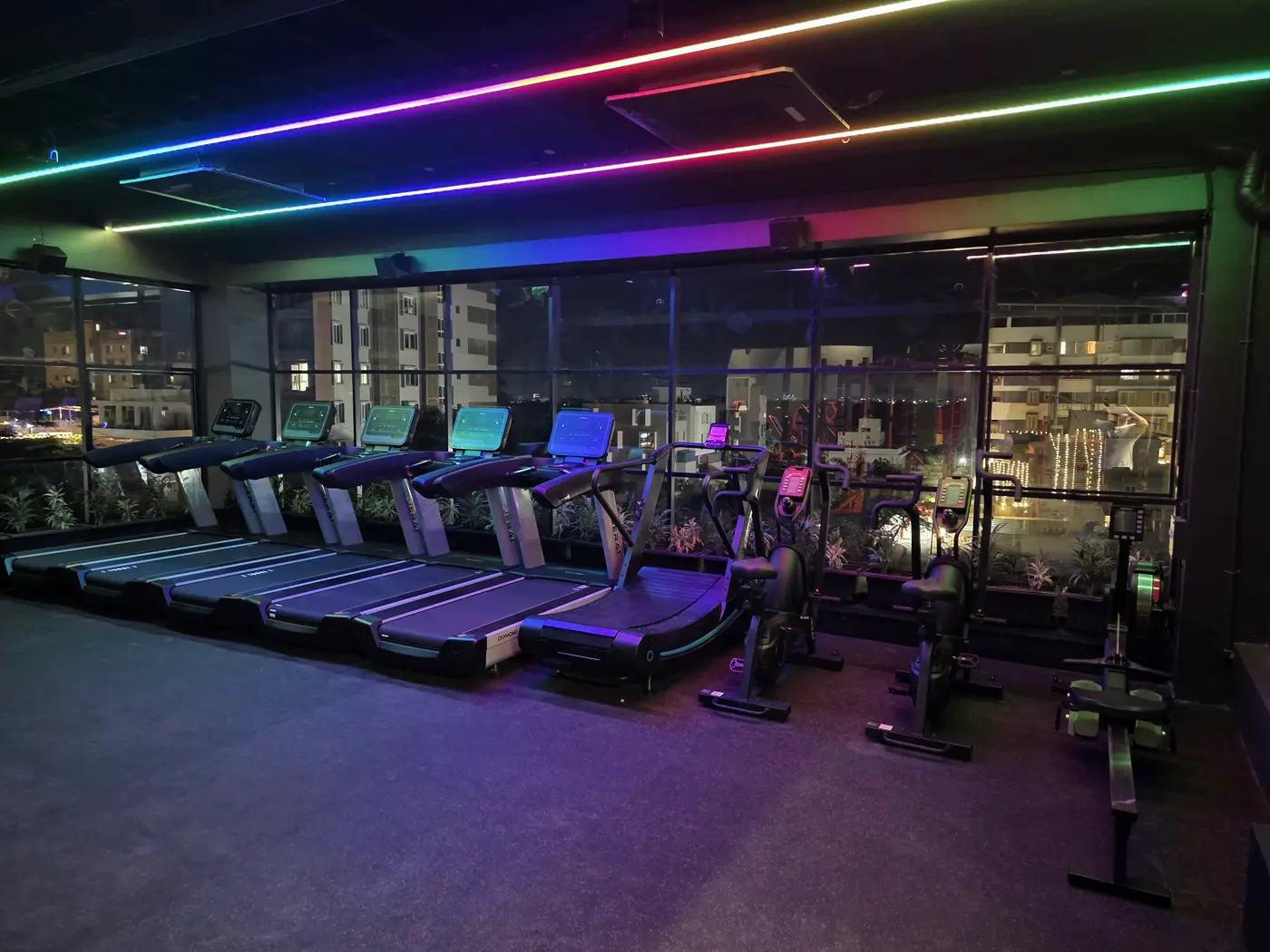 The same Floor 2 cardio line under colour lighting synced to the music